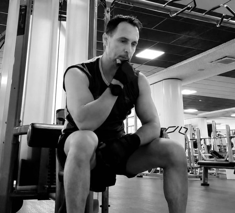 Hombre en el gimnasio, sentado y pensativo, con guantes de entrenamiento.